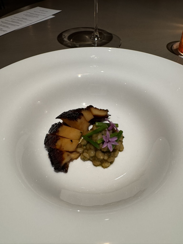 Grilled seafood course plated with grains and a purple flower