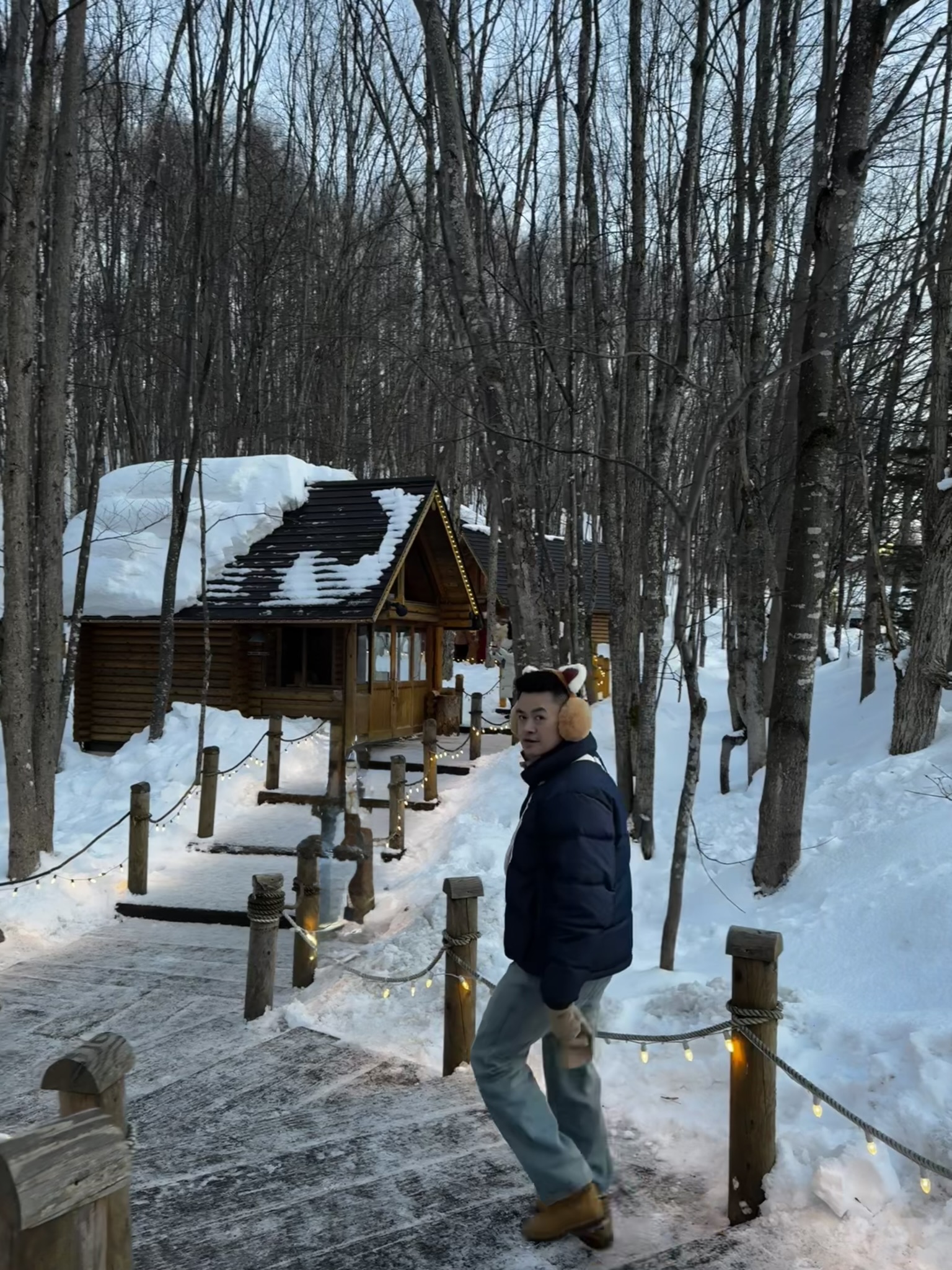 Walking through snowy Ningle Terrace with wooden cabins and lights