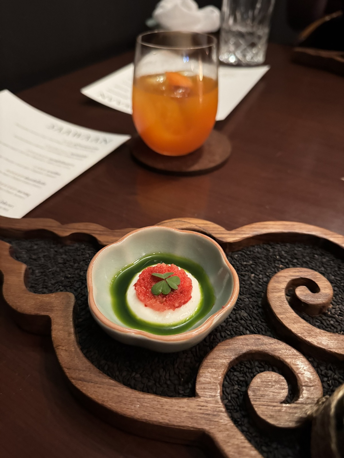 A Saawaan course with green leaves and a yellow garnish in a ceramic bowl on a carved tray