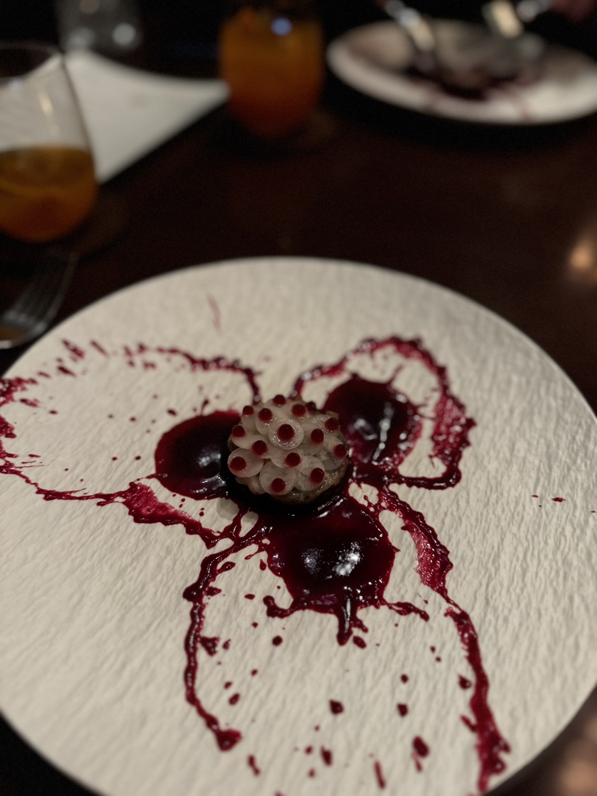 A red-toned Saawaan course with dramatic sauce on a textured white plate
