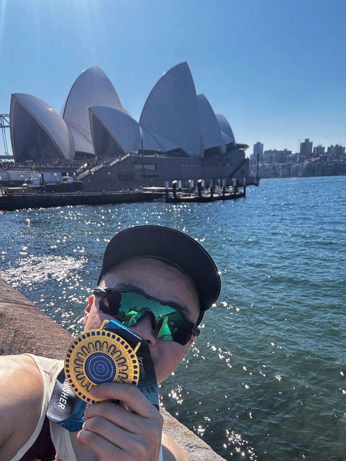 Finisher holding a Sydney Marathon medal with the Opera House behind