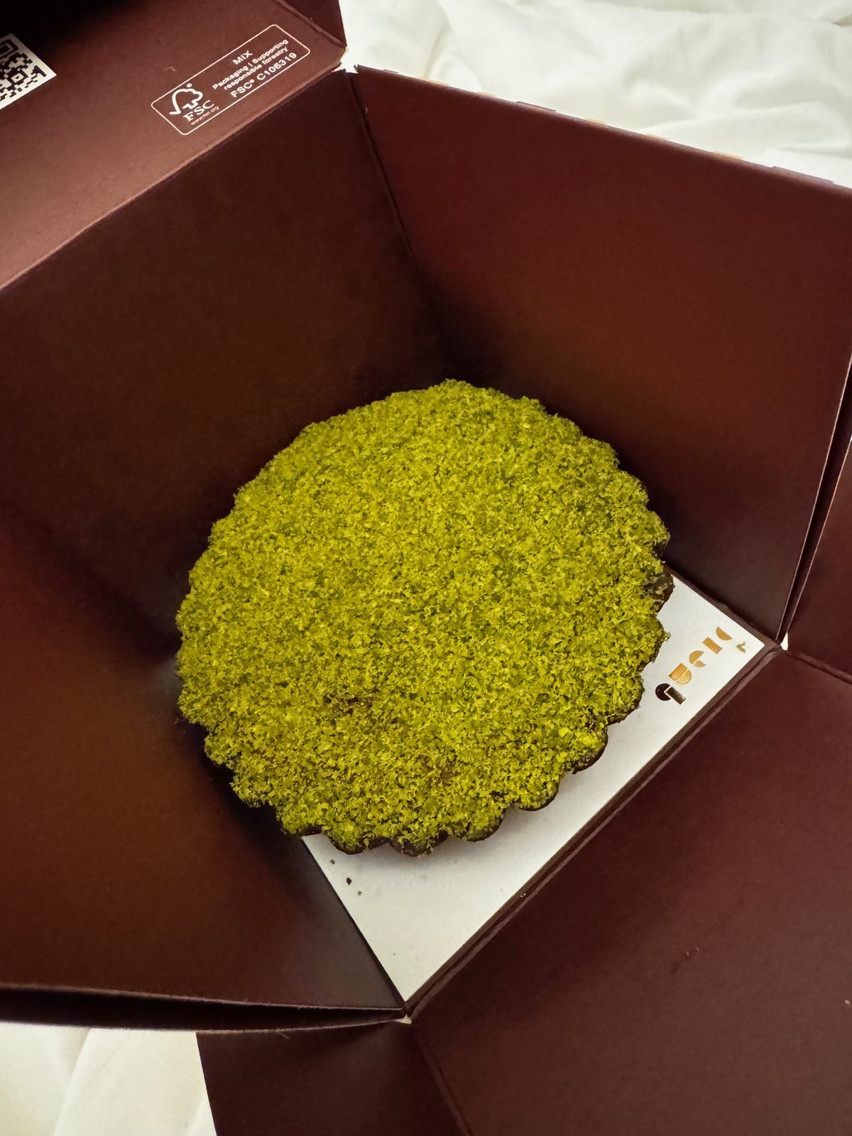 Green-topped cheesecake in an open box on a bed at night